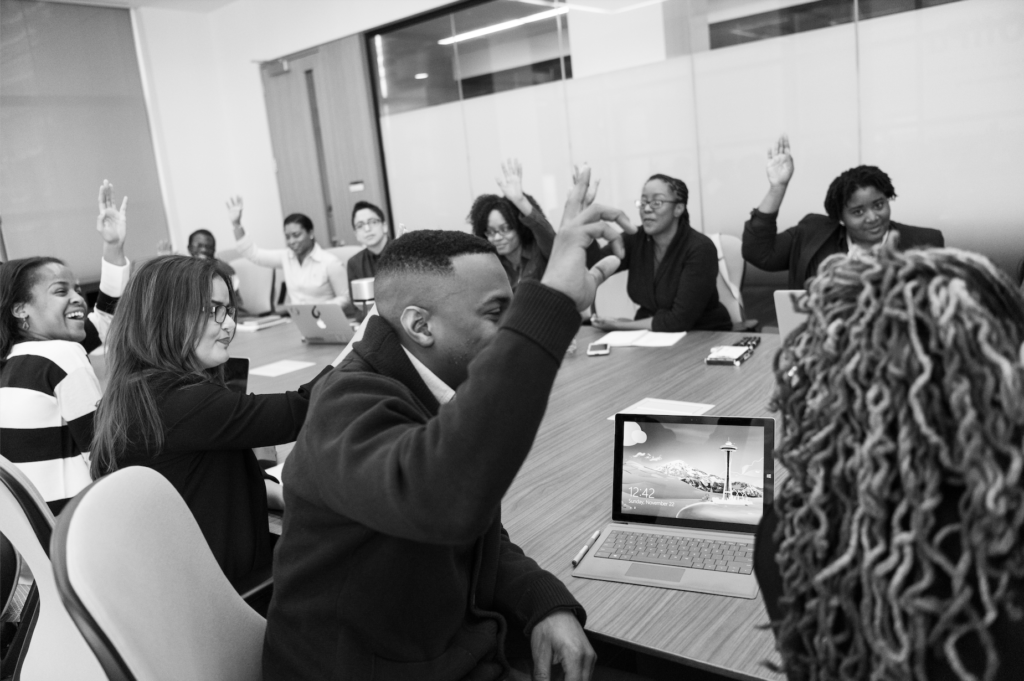 Black and white photo of Black and brown young professionals enthusiastically participating around a boardroom style table