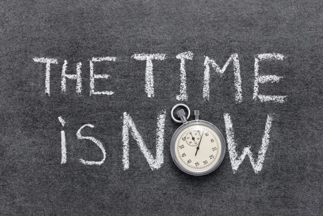 Image is in the style of a blackboard with the words "the time is now" in white chalk, and the "o" in "now" a stopwatch
