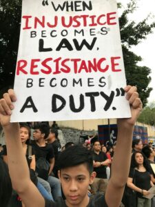 protestor holds up a sign saying "when injustice becomes law, resistance becomes a duty."