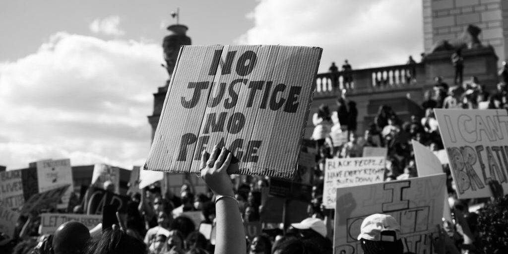 black and white photo of crowd of protesters holding signs No Justice No Peace in center